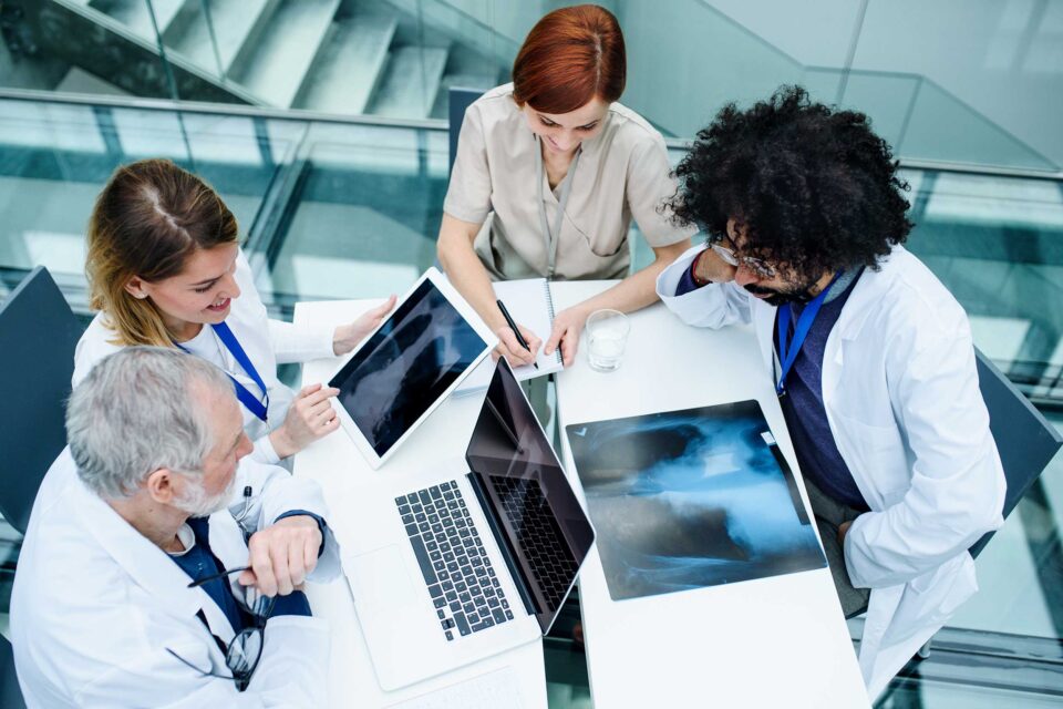 Group of doctors in white coats sitting together at a table reviewing xrays on their computers Oceania University of Medicine